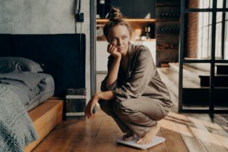 Young dissatisfied unhappy woman crouched over electronic scales